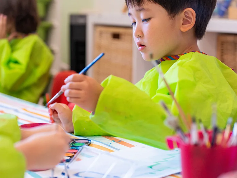 A child in a smock drawing during the morning activity